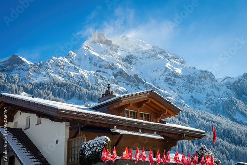 Adelboden, Switzerland - January 12, 2025: A traditional Swiss chalet decorated with national flags for Ski Alpine World Cup at Chuenisbärgli with Lohner Mountains in the background against blue sky