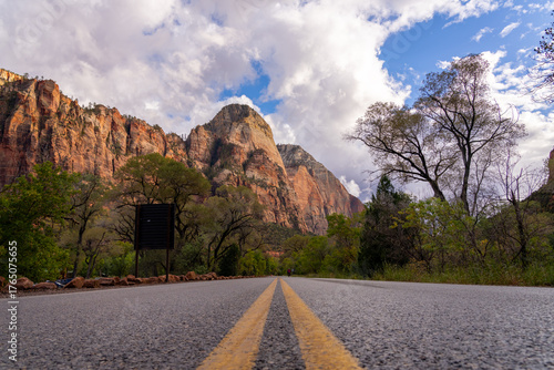 Road leads to majestic sandstone cliffs under cloudy sky.