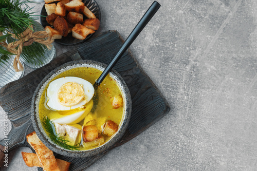 Half an egg in a spoon served with chicken or turkey broth. Broth with egg and crackers. Top view, close-up. Copy space