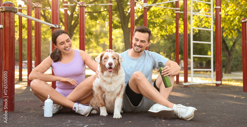 Young couple with Australian Shepherd dog sitting on sport ground
