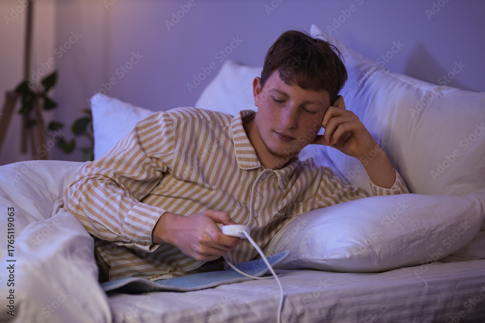 Fototapeta premium Young man turning on electric heating pad in bedroom at night