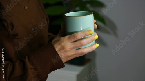 Closeup hands video of business woman holding in hands mug with coffee and relax drinking in office, room interior with green flower. Business concept	
