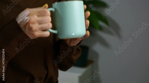 Closeup hands video of business woman holding in hands mug with coffee and relax drinking in office, room interior with green flower. Business concept	
