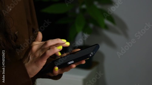 Closeup hands video of business woman holding in hands mobile phone and working, texting, chatting in office, room interior with green flower. Concept	
