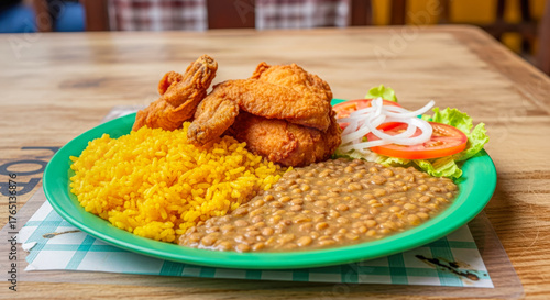 Traditional Latin American dish featuring yellow rice, baked beans, crispy fried chicken, and a fresh tomato and onion salad.