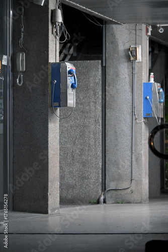 Taipei, Taiwan - Sep.  29, 2025: Public payphone with blue panel and white handset mounted on gray wall, door ajar, cable hanging overhead in interior corridor, National Taiwan University campus.