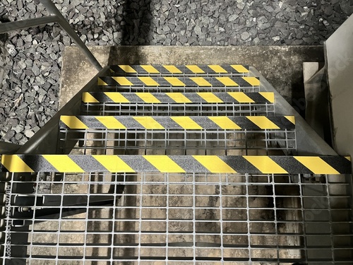 Metal grating staircase steps feature prominent yellow and black diagonal anti slip safety tape