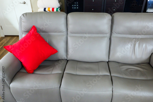 A bright red decorative pillow on the left end of a gray sofa.