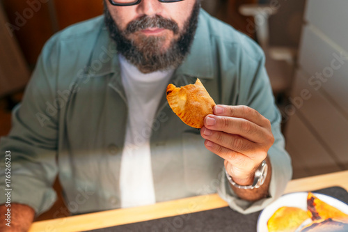 Quadro su tela Man holding bitten empanada while sitting at desk.