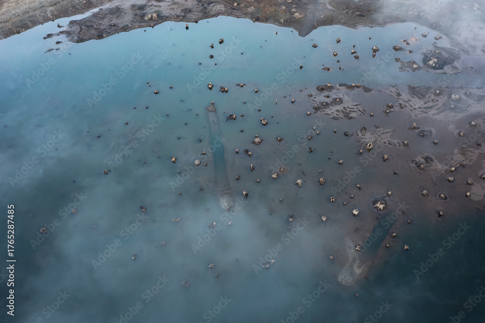 Fototapeta premium Aerial drone picture of Wynoochee Lake in Olympic National Forest, Washington State, USA, showing fog over turquoise water with visible submerged tree roots and stumps emerging from the surface 