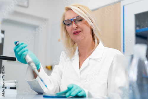 Bilde på lerret Female biochemist using a pipette to prepare agar media in a petri dish