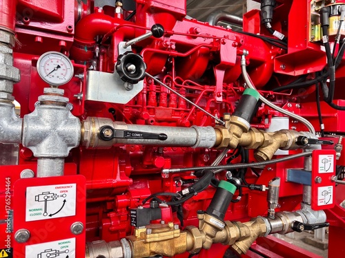 Close-up of a bright red industrial fire pump system with silver and brass piping, pressure gauges, and control valves, essential for fire suppression and safety.