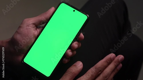 Man's hand holding a smartphone with green screen