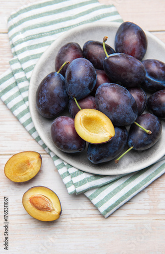 Fresh ripe plums in grey bowl on wood table