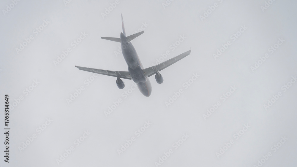 Fototapeta premium A plane is flying through a cloudy sky. The sky is overcast and the plane is low to the ground