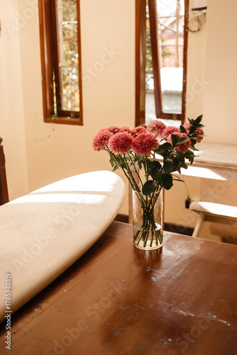 Pink chrysanthemums in a glass vase on a background of white surfboard. Flowers in the surfer living room. Bouquet of flowers in the interior of the house