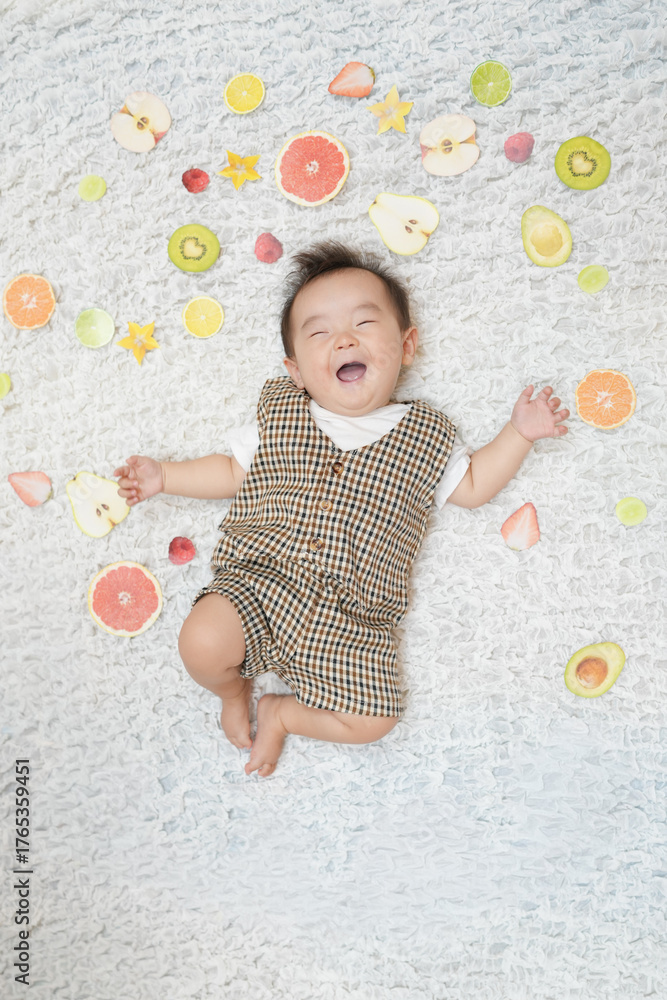 Fototapeta premium A baby is laying on a bed with a variety of fruits surrounding him. The baby is smiling and he is enjoying the fruits. Concept of happiness and playfulness