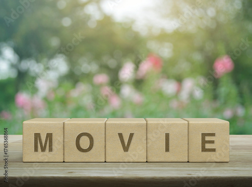 Movie letter on wood block cubes on wooden table over blur pink flower and tree in garden, Business cinema online concept