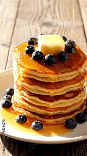 Pouring Maple Syrup on Stack of Pancakes Topped With Blueberries and Butter