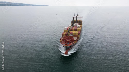 Aerial view of a large cargo ship carrying colorful containers approaching the port. Maritime transport and international shipping concept