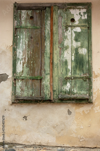A closed wooden, old, scratched shutter with peeling paint and a fragment of the old facade of the building. Architecture.