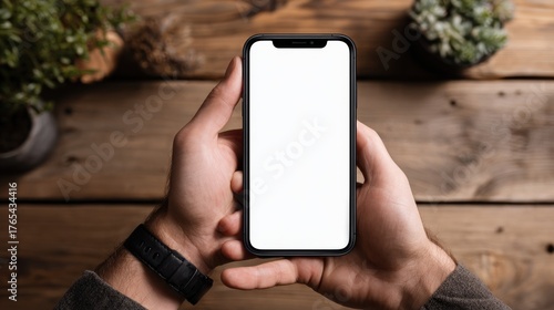Hands holding smartphone with blank screen on wooden table background