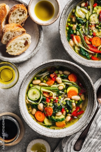 Two bowls of vibrant vegetable soup, garnished with fresh herbs, alongside slices of crusty bread. Olive oil drizzles visible