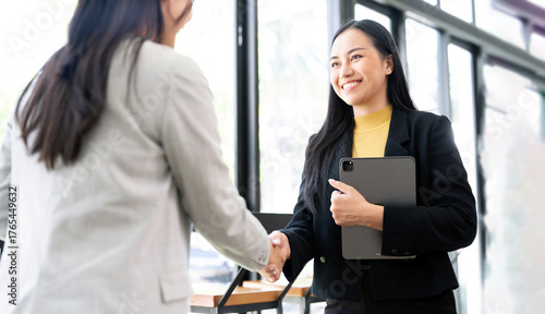 Two Asian businesswomen finalize a deal with a firm handshake in the office.