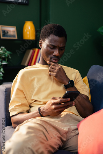 Young man using phone thinking decision on couch