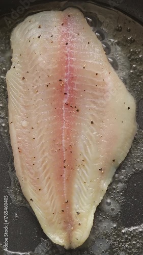 Pan-frying raw pangasius dory fish fillet on a hot pan. Top view shot