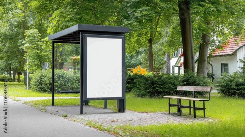Modern outdoor park display board with blank advertising space next to bench on lush green sidewalk in sunny urban environment