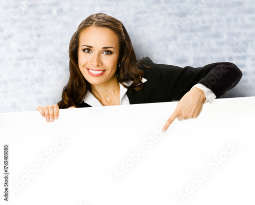 Happy smile woman in black corporate suit peep out show pointing advertise blank white banner signboard with empty sign text free space. Business ad concept. Stand against white bricks wall background