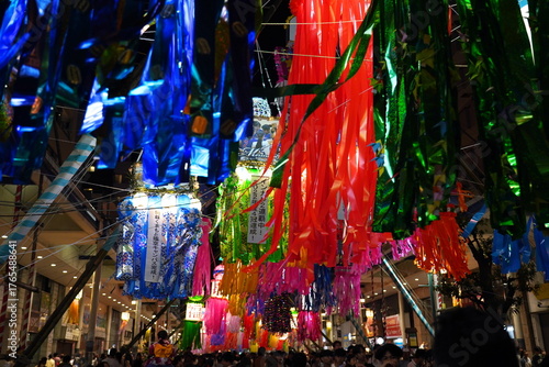 Fotografija 夜の商店街の頭上に赤青緑など極彩色の七夕飾りが密集して吊るされお祭りの熱気と賑やかさを感じさせます