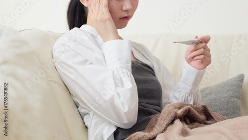 体温計で熱を測るアジア人女性