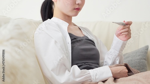 体温計で熱を測るアジア人女性