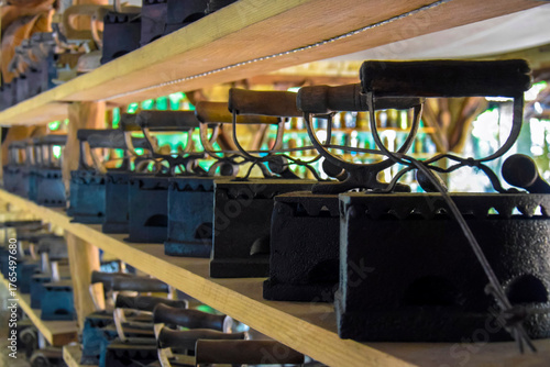 A collection of antique irons on shelves in street cafe. Rows of vintage cast iron products. Unusual decoration of restaurant. Copy space. Selective focus.