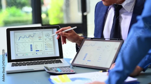Closeup of professionals analyzing financial data on laptop and tablet in modern office, symbolizing teamwork, analytics