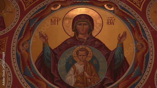 A close-up of a golden Orthodox icon depicting the Holy Mother of God with the Child Jesus Christ. Traditional church wall painting in warm light, symbol of faith and divine protection.