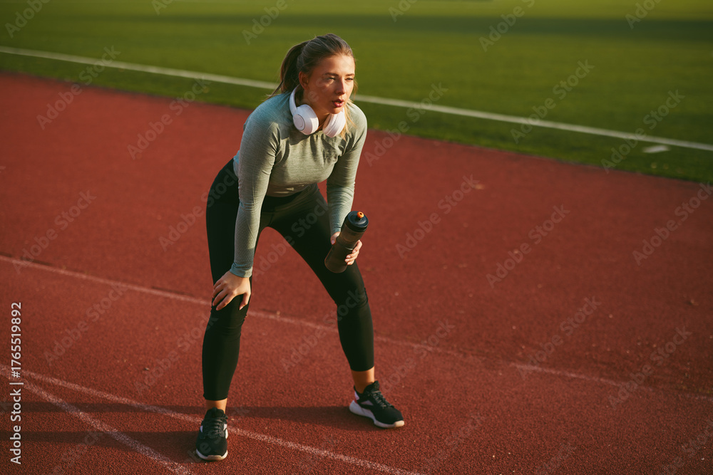 Obraz premium Young woman resting after workout on a track, holding a water bottle