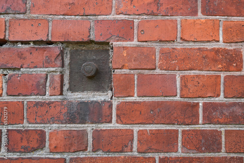 A close-up of an antique brick wall with a steel fastening element. The metal nut and square plate are rusted with age. Background. Texture.