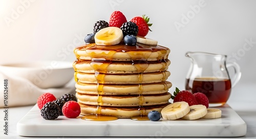 Stacked pancakes with fresh berries, banana slices, and maple syrup