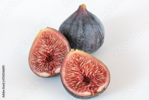 Whole and halved Black Mission figs displayed on a clean white background, showcasing the fruits deep purple skin, soft texture, and vibrant red interior, fresh produce used in Mediterranean cuisines