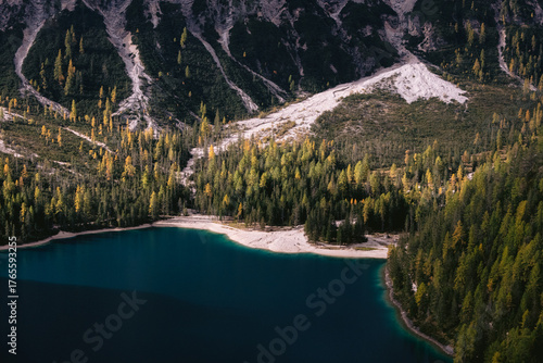 Aerial view of the dark blue lake reflecting the sky, contrasting with the yellowing trees and rugged mountains, creating a serene yet dramatic landscape, Prags, Trentino-South Tyrol, Italy.