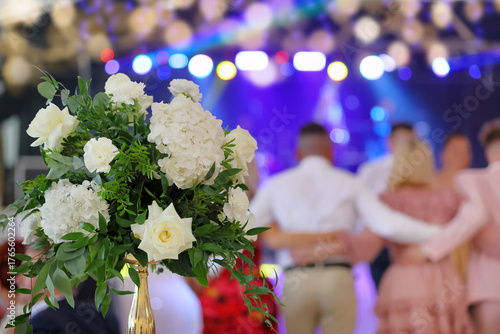 Bride's wedding bouquet and dancing couples at the wedding reception in the background.