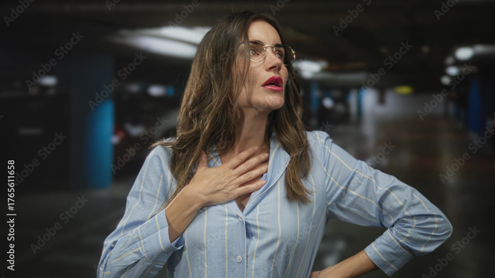Fototapeta premium Woman wearing glasses holds neck next to car in an underground parking garage looking concerned; anxiety.