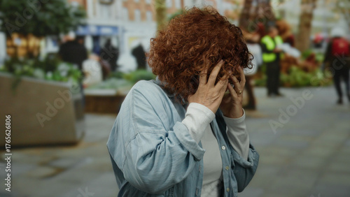 Foto Woman with curly hair appearing worried on a bustling city street with people and greenery, middle-aged and brunette in urban outdoor setting with a concerned expression