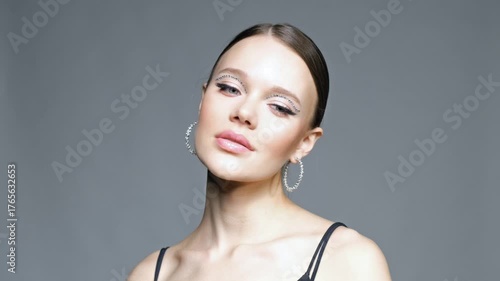 Video of female with rhinestones face makeup and earrings in the form of a shiny ring.