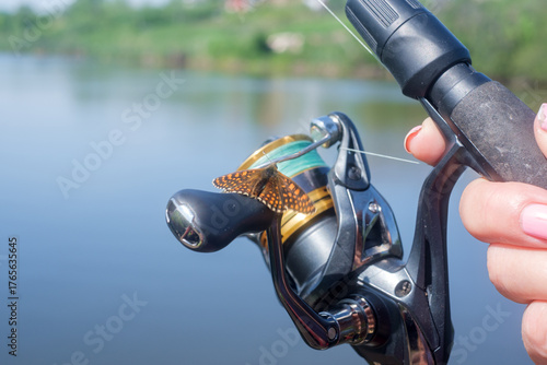 A butterfly sits on a spinning reel in a woman's hand