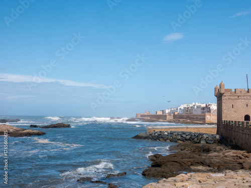 Historic Ramparts of Essaouira Fortress Rising from the Rocky Atlantic Coast, with Crashing Waves Under a Vibrant Blue Sky in Morocco