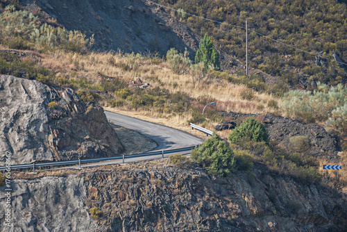 A secondary road winds between hills covered in heather and gorse with views of mountain ranges on the distant horizon.